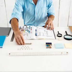 Hands of young businessman sitting at table with notepad. White modern office background.